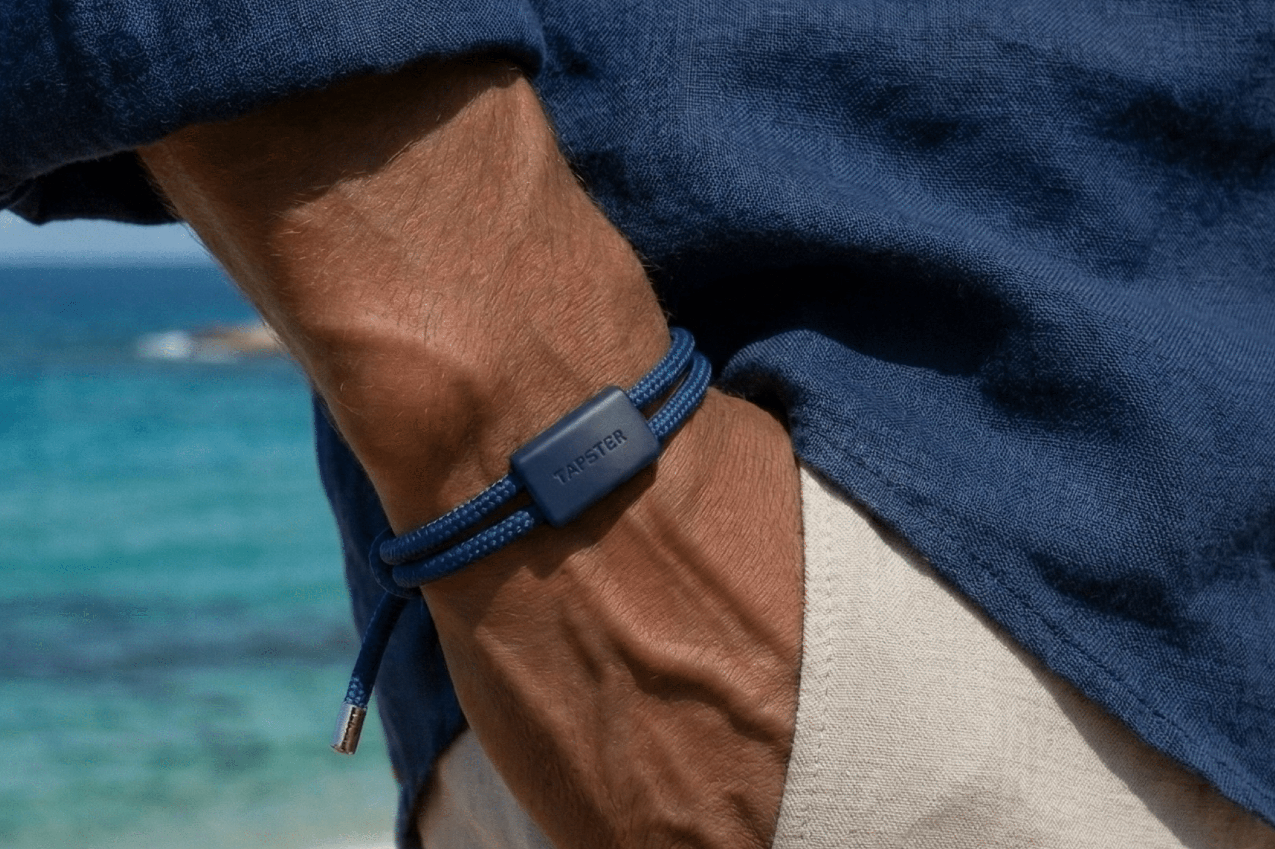 Person med blått Tapster-armbånd på håndleddet ved sjøen.