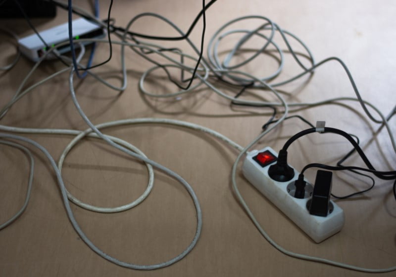 Et virvar av kabler og en skjøteledning på et lyst tregulv