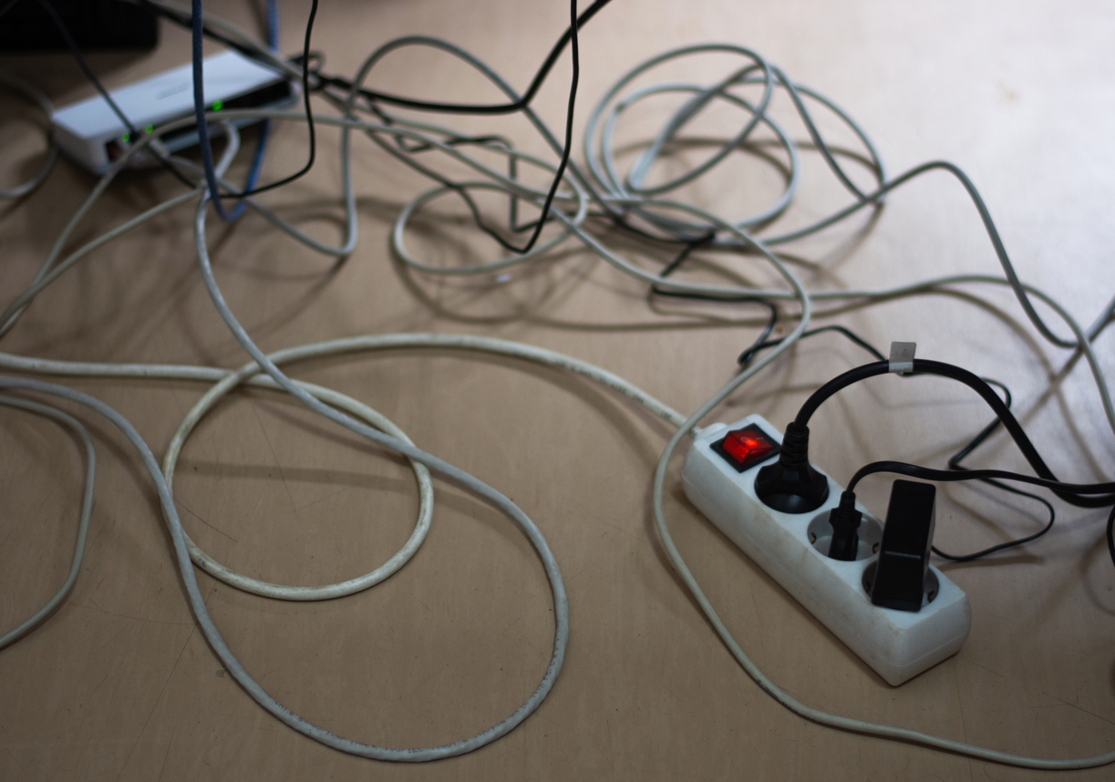 Et virvar av kabler og en skjøteledning på et lyst tregulv
