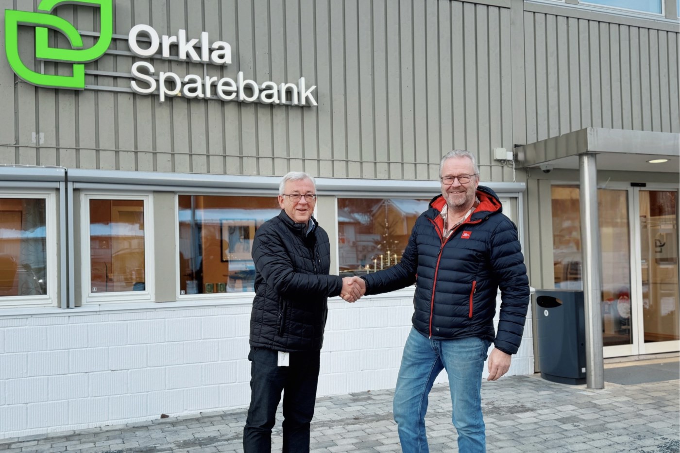 Arnt Ree, rådgiver i Orkla Sparebank håndhilser på en fornøyd Kjell Berdal, daglig leder i Lium, utenfor banken.